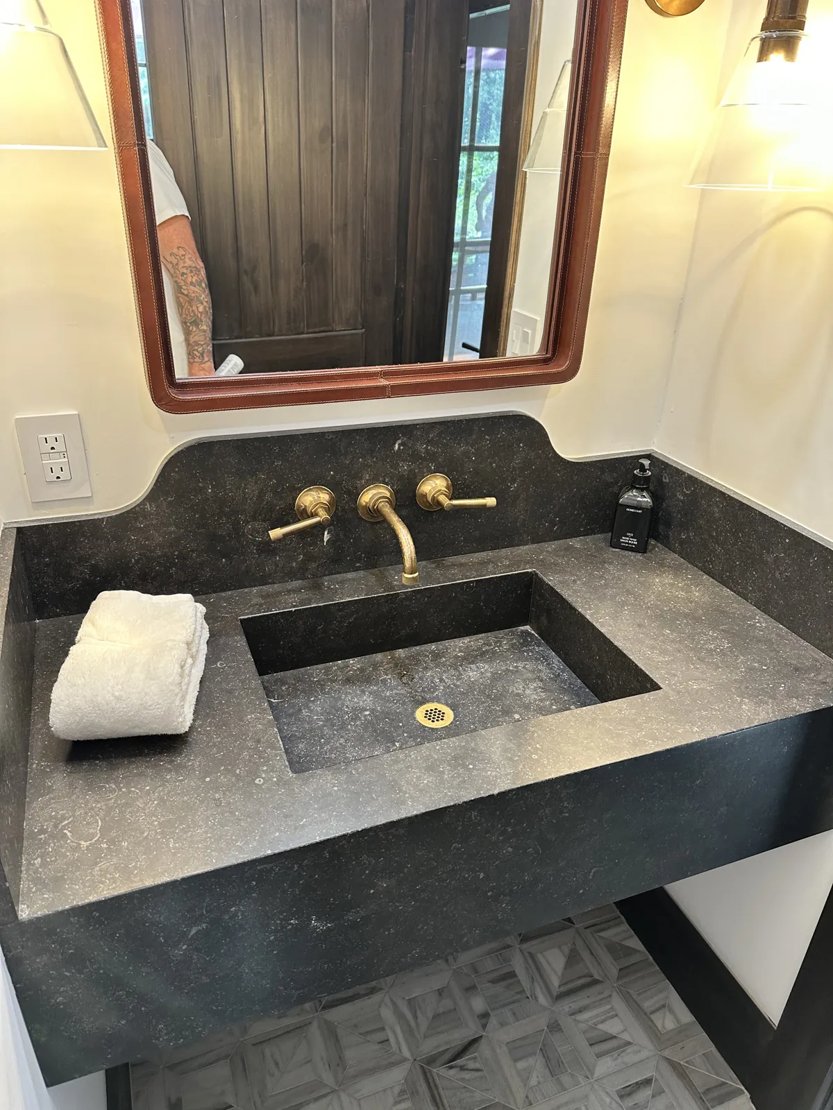 Floating black limestone powder room vanity with an integrated sink and brass wall faucet in a Lake Tahoe home